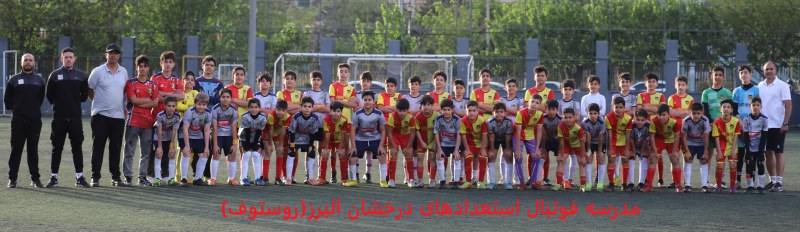 عکس دوستانه دو تیم فوتبال نوجوان یکی با لباس طلایی و آرم روستوف و دیگری قرمز در زمین چمن به همراه مربیان