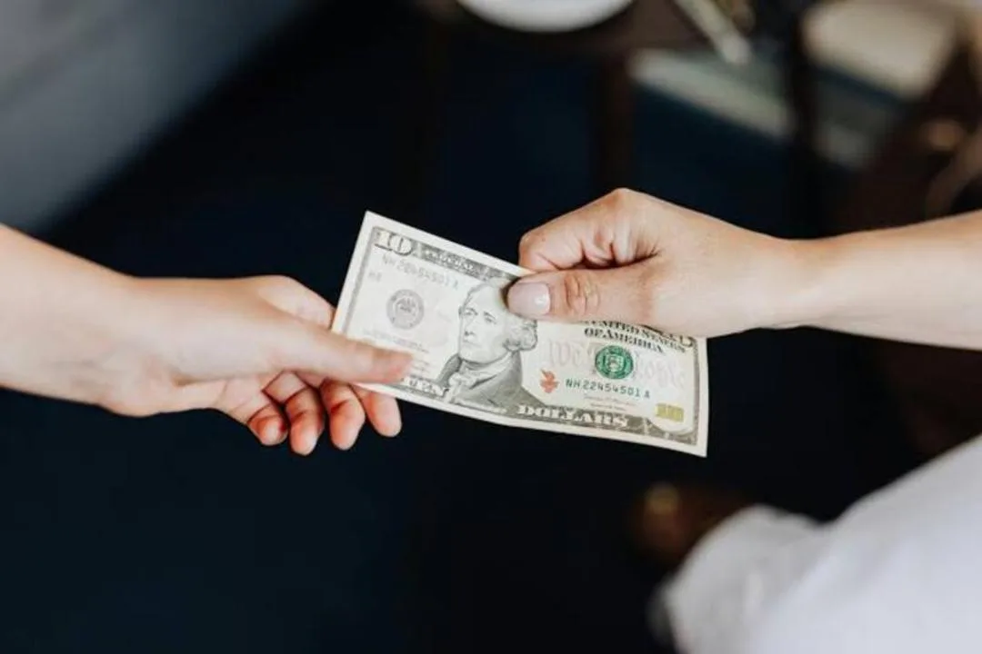 دستهای دو نفر در حال رد و بدل کردن اسکناس یک دلاری آمریکا (United States Dollar)